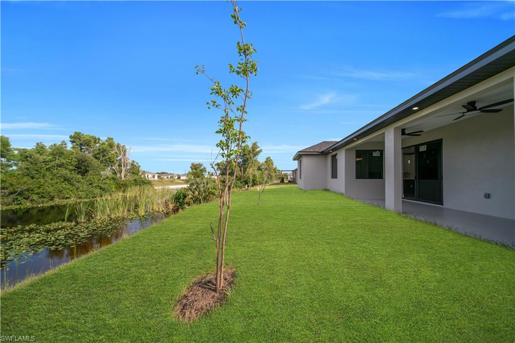 Expansive green lawn with a water feature, covered patio, recessed lighting, and ceiling fans