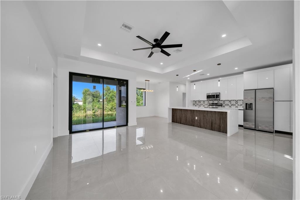 Open-concept living space with light gray tile flooring, a tray ceiling, and a ceiling fan
