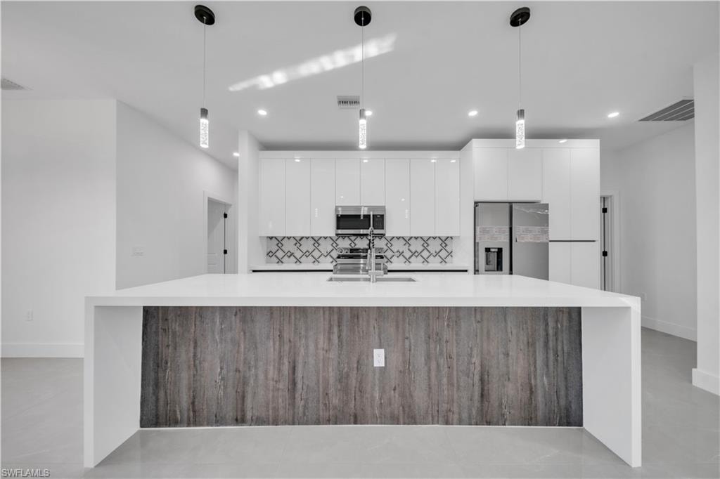 Contemporary kitchen featuring a large island with white countertops, integrated stainless steel appliances, and sleek white cabinetry