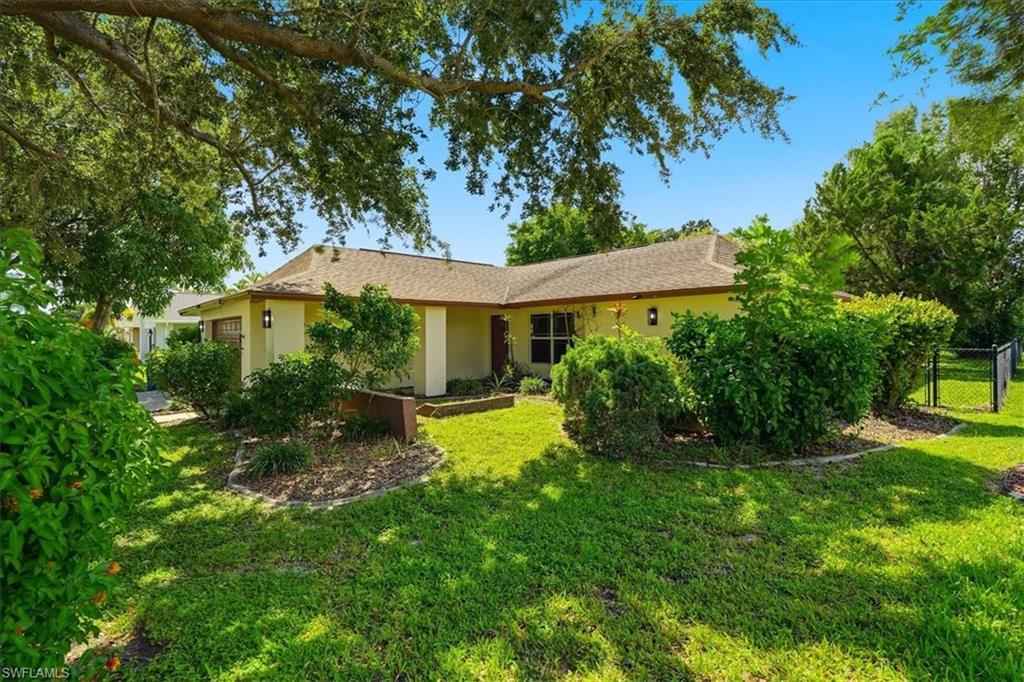 Stucco exterior with a shingle roof, mature landscaping, and a fenced yard