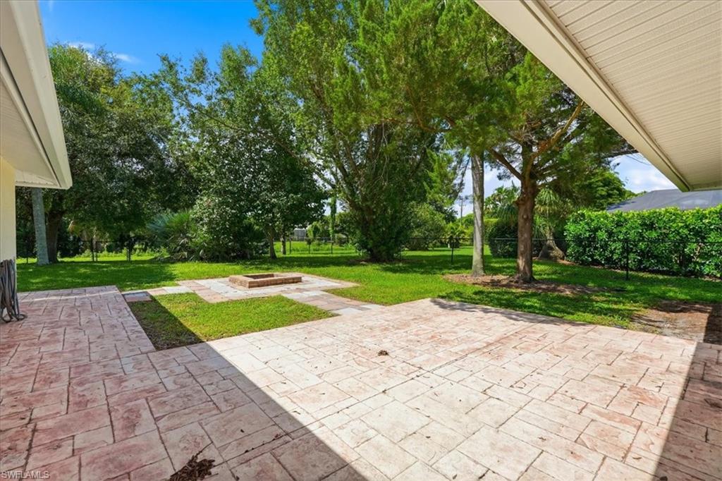 Expansive backyard featuring a stamped concrete patio, a built-in fire pit, lush green lawn, mature trees, and privacy hedging