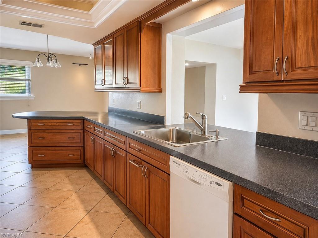 Kitchen featuring wood cabinetry, dark countertops, a stainless steel sink, a built-in dishwasher, and tiled flooring
