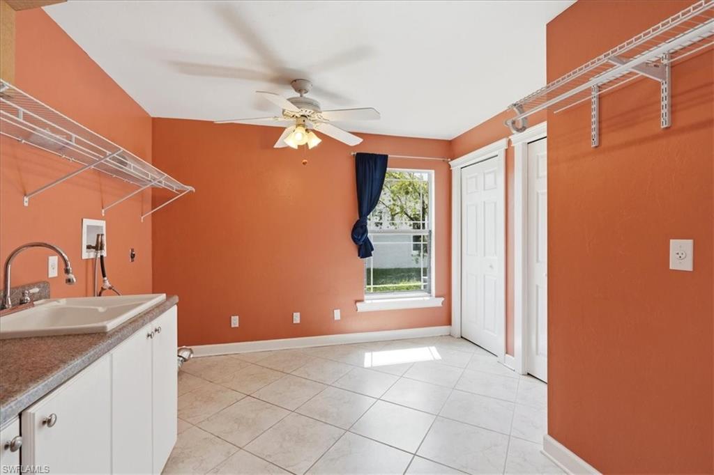 Utility space featuring tile flooring, a built-in sink with a countertop, white cabinetry, and ceiling fan