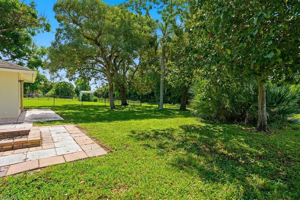 Expansive lawn area with mature trees, brick paver patio, and stone fire pit