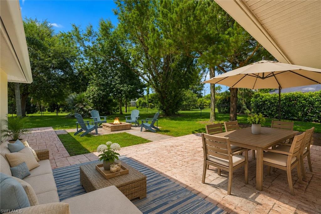 Expansive stamped concrete patio with fire pit, shaded outdoor dining area, and lush green lawn