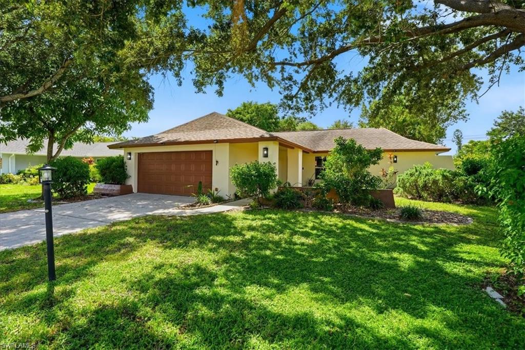 Stucco exterior with a hip roof, attached garage with a panel door, concrete driveway, and established landscaping