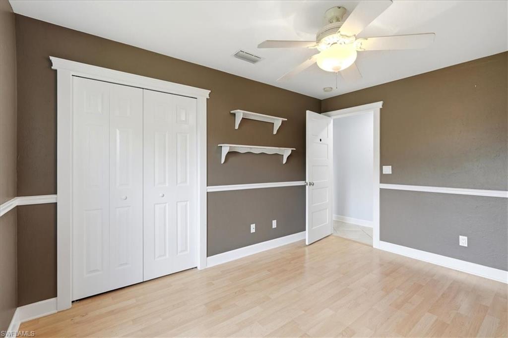 Wood-finish flooring, white bi-fold closet doors, ceiling fan, and crown molding