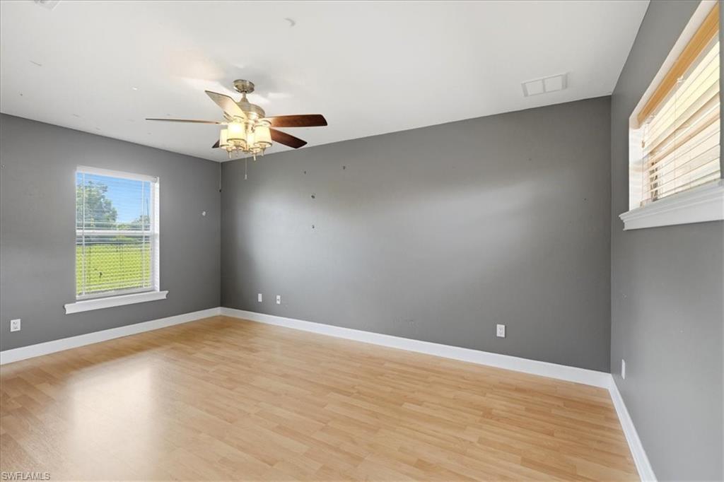 Wood-finish flooring, ceiling fan with integrated lighting, multiple windows, and white trim