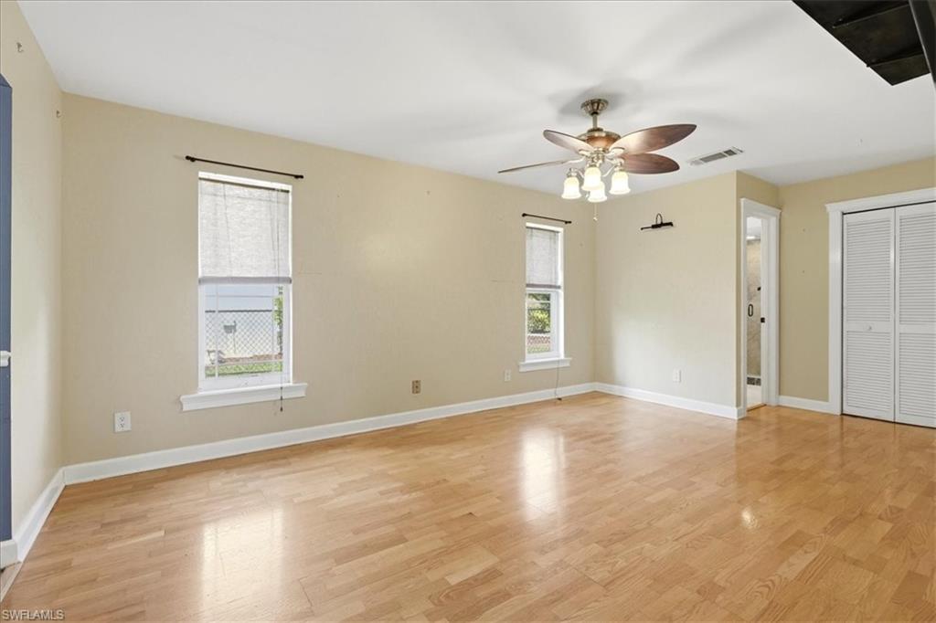 Expansive room featuring light wood-finish flooring, multiple windows, a ceiling fan with integrated lighting, and louvered bifold closet doors