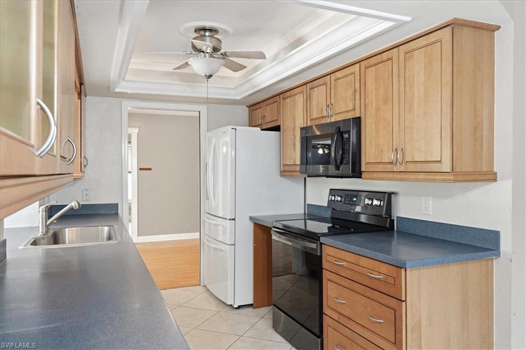Wood-finish cabinetry, dark countertops, tile flooring, stainless steel sink, and ceiling fan with light fixture