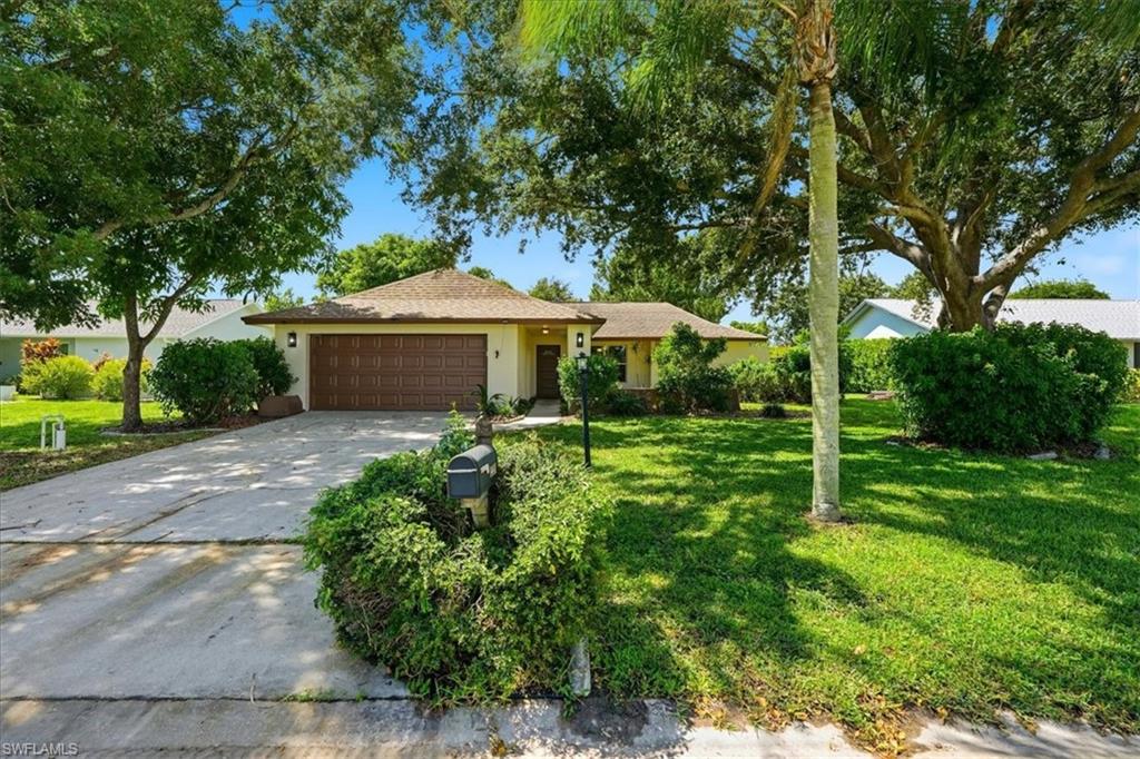 Front exterior with an attached two-car garage, mature trees, manicured lawn, and lush landscaping