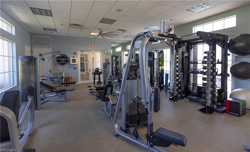 Exercise room featuring ceiling fan, a drop ceiling, and plenty of natural light