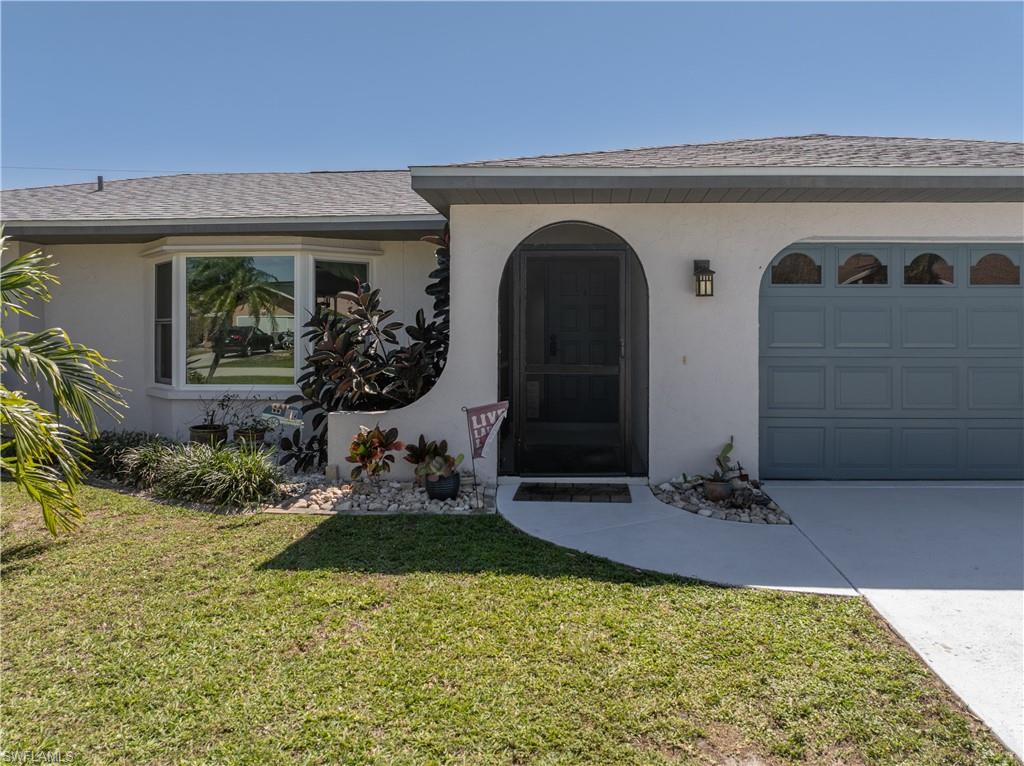 View of exterior entry with an attached garage, a yard, roof with shingles, and stucco siding
