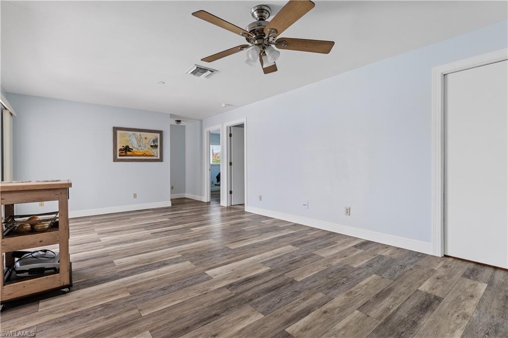 Empty room with a ceiling fan, wood finished floors, visible vents, and baseboards