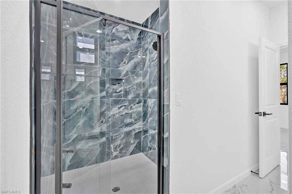 Glass-enclosed shower with blue-toned tile, recessed wall niche, and black-framed fixtures