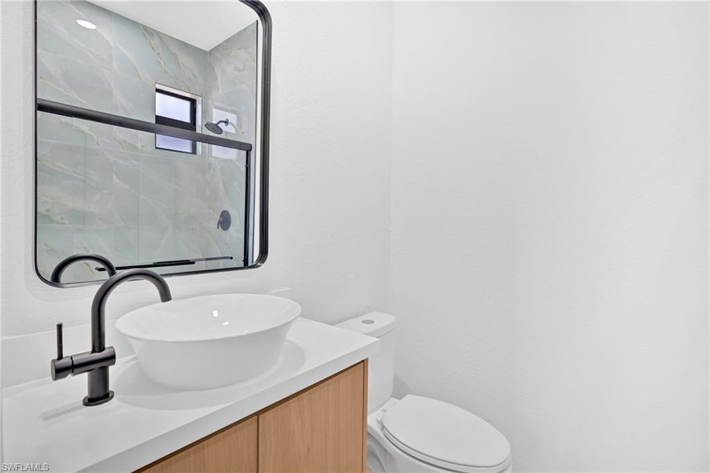 Modern vanity with wood-finish cabinetry, white countertop, vessel sink, and matte black faucet