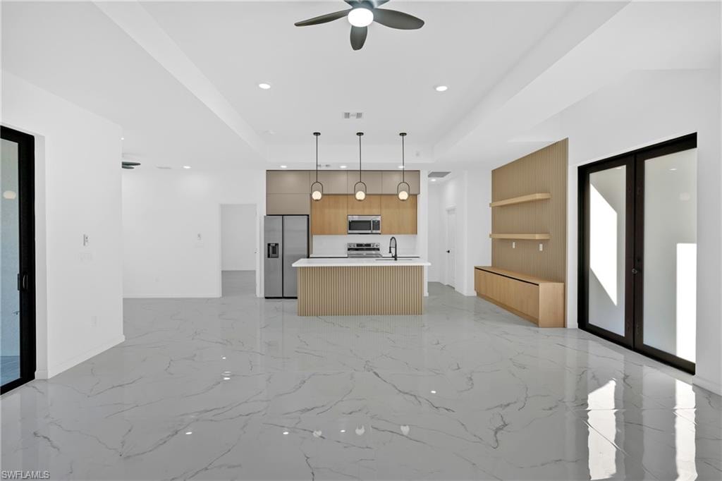 Open-concept interior featuring large format tile flooring, a modern kitchen with a center island, pendant lighting, and a built-in media console with shelving