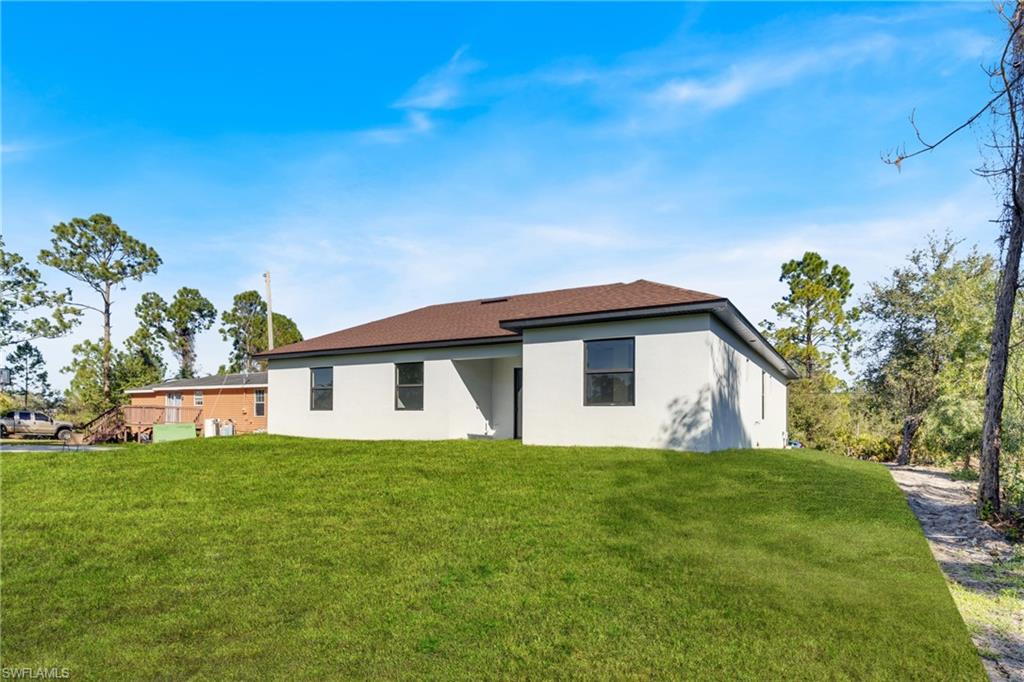 Newly constructed residence featuring a neutral stucco exterior, dark-framed windows, and a brown shingle roof