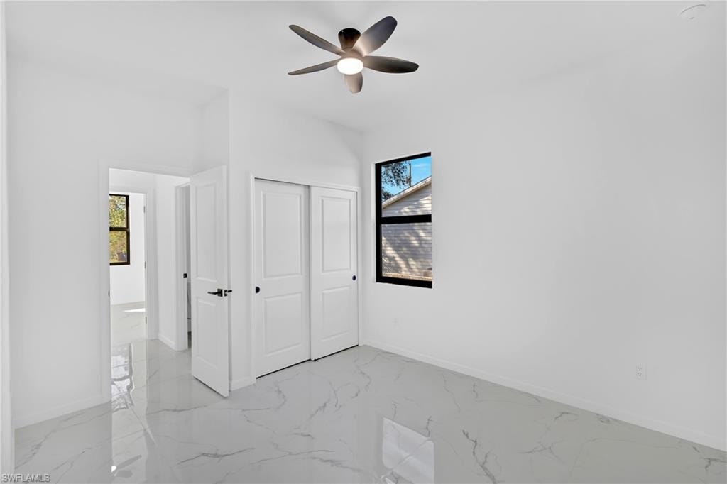 White walls, two white panel doors, black framed window, and a ceiling fan with integrated lighting