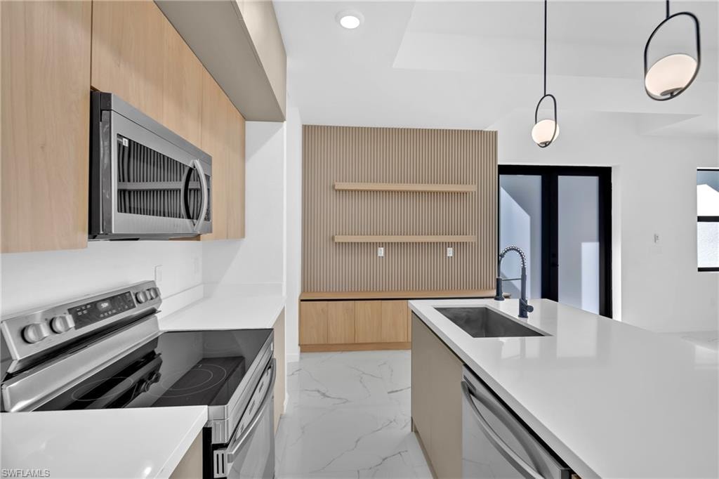Modern kitchen featuring light wood-finish cabinetry, stainless steel appliances, a center island with an undermount sink, and white countertops