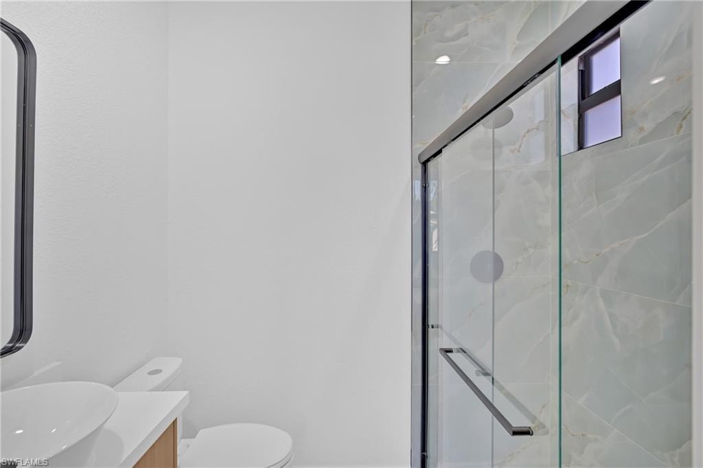 Sliding glass shower enclosure with chrome hardware, full-height decorative tile, and a white vanity with an integrated basin sink