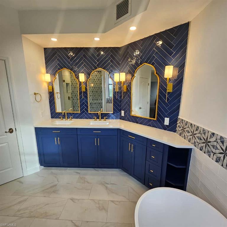 Full bath with tile walls, double vanity, a freestanding tub, and marble look tile flooring