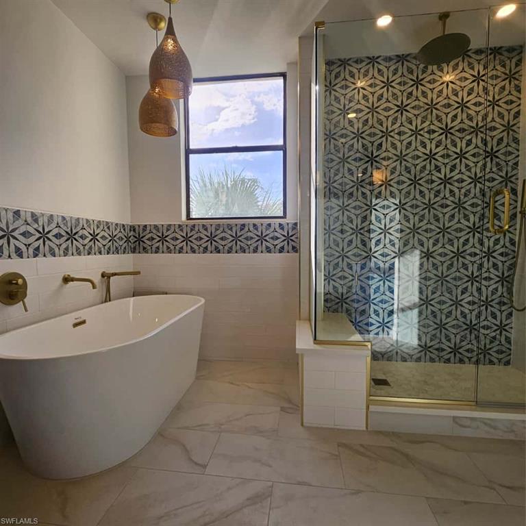 Full bath with a freestanding bath, a tile shower, tile walls, and marble finish flooring