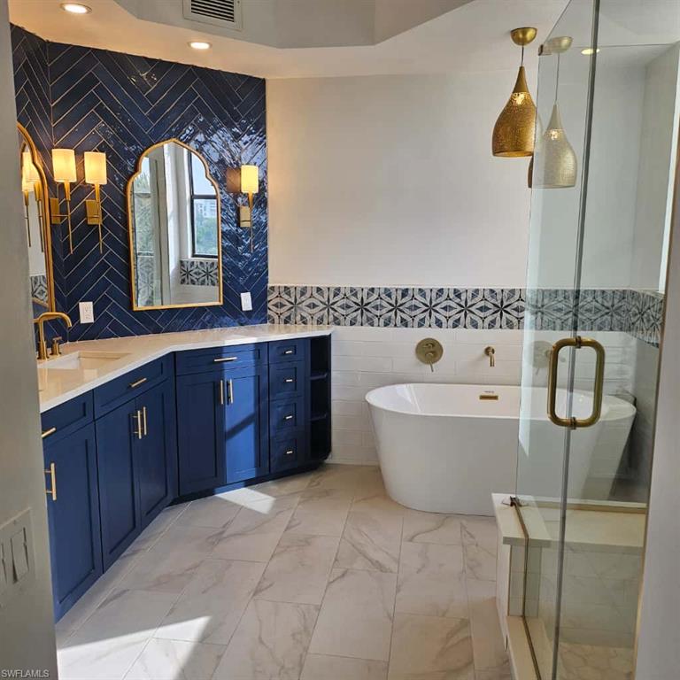 Full bathroom featuring tile walls, vanity, a freestanding tub, marble finish floors, and a stall shower