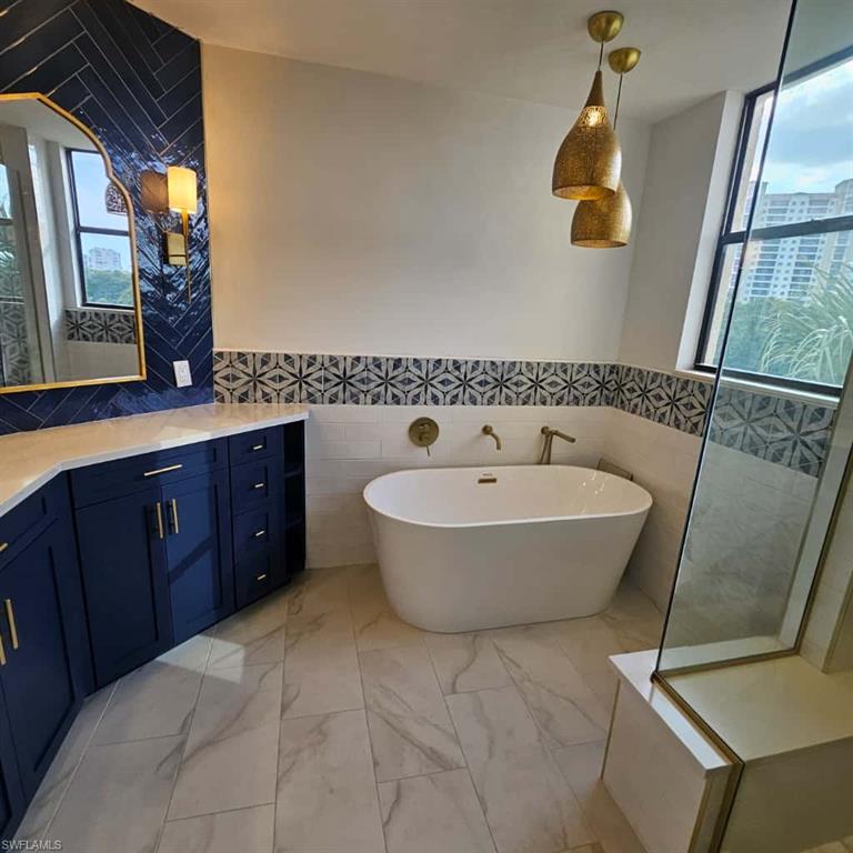 Bathroom featuring healthy amount of natural light, tile walls, a soaking tub, vanity, and marble finish flooring
