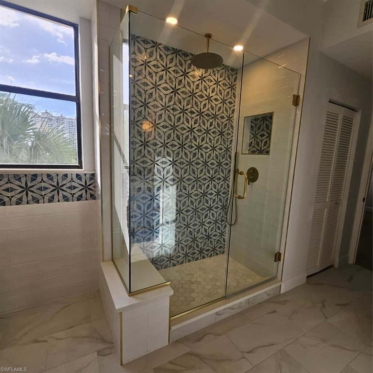 Full bath with marble look tiles, a stall shower, and a closet