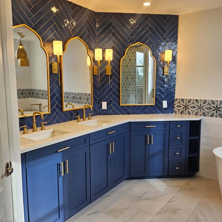 Full bath featuring tile walls, a freestanding bath, double vanity, and marble look tiles