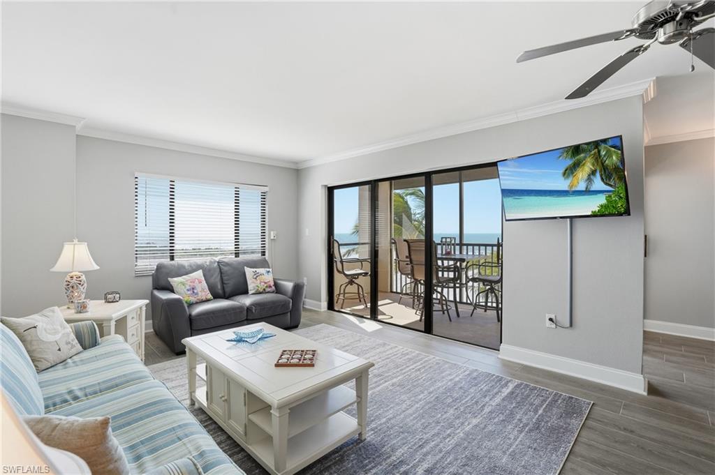Living room with ceiling fan, wood finished floors, crown molding, and plenty of natural light
