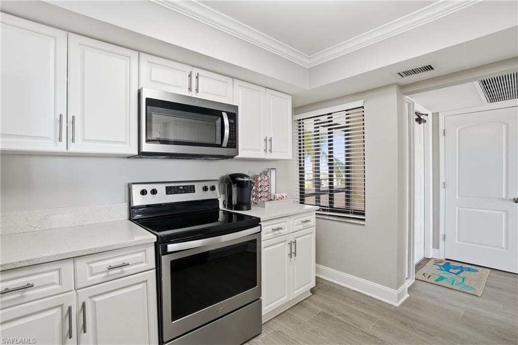 Kitchen featuring stainless steel appliances, white cabinets, crown molding, light wood-style flooring, and light stone counters