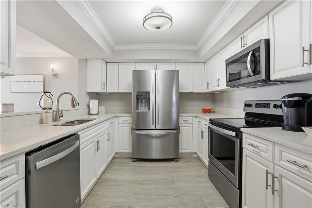 Kitchen with stainless steel appliances, light stone countertops, white cabinets, crown molding, and light wood-type flooring
