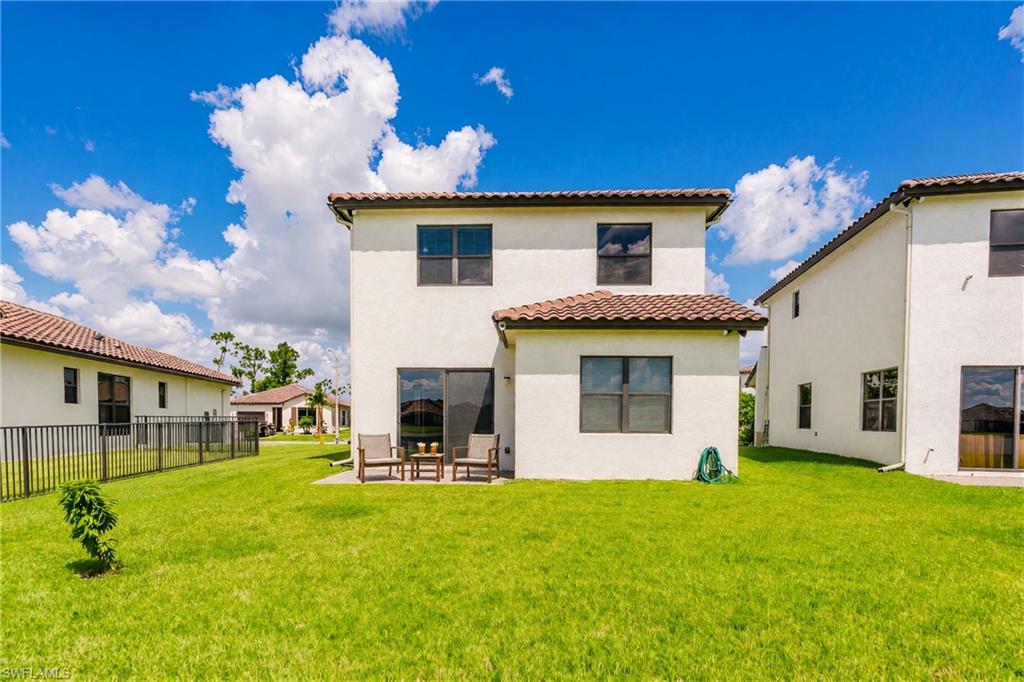 Expansive green lawn, stucco exterior, multiple windows, sliding glass door, and a tiled roof