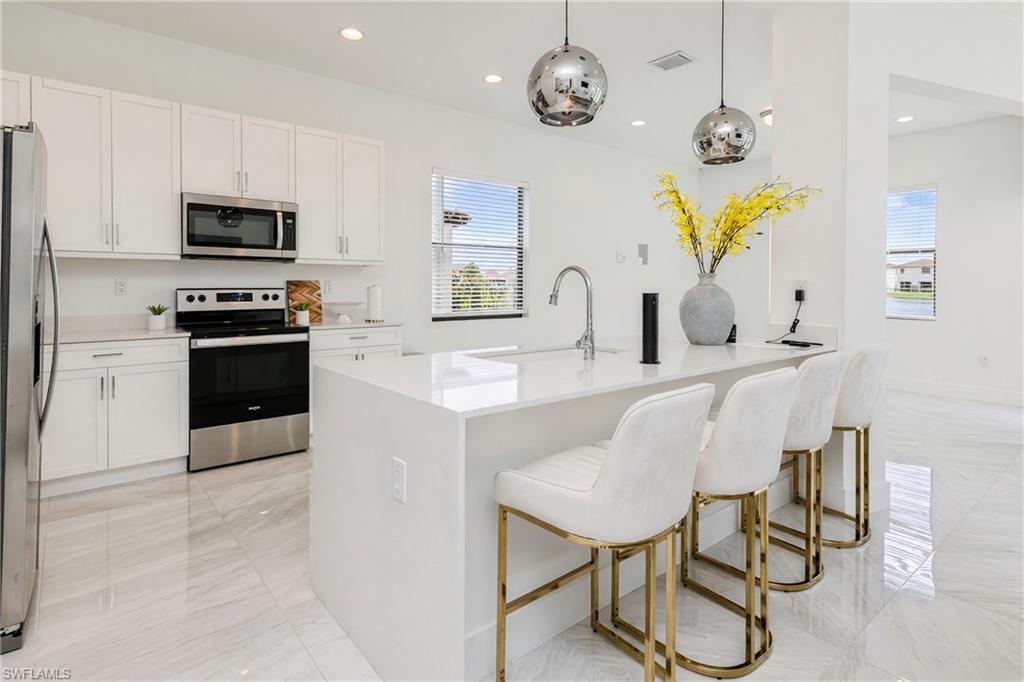 Kitchen featuring stainless steel appliances, white cabinetry, a large center island with a sink, and polished tile flooring