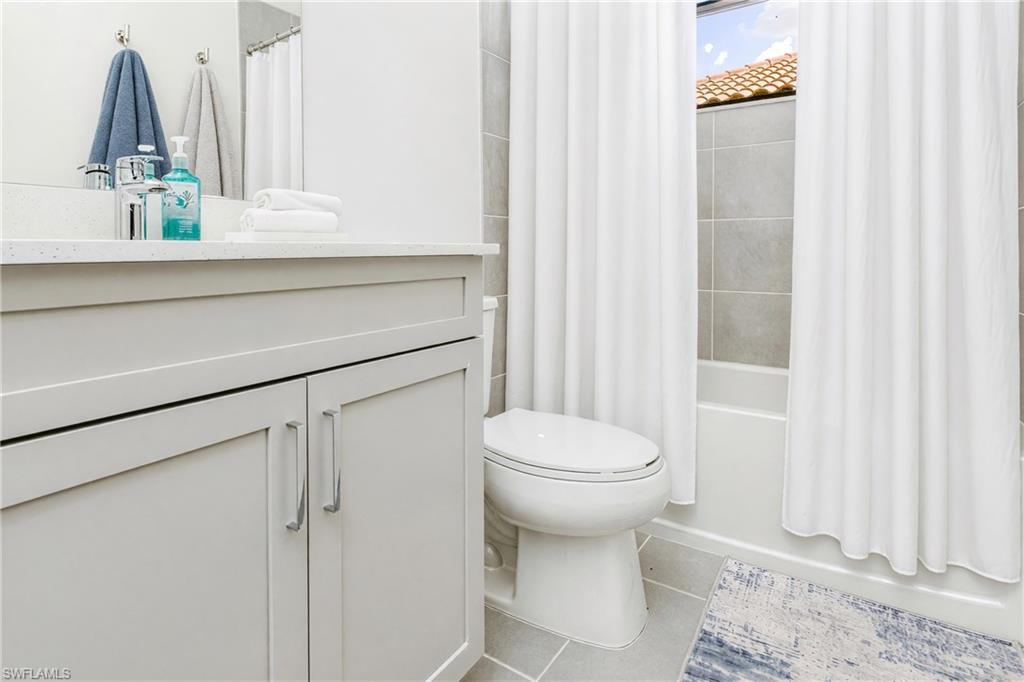 White vanity with a light-colored countertop, chrome faucet, and tiled shower surround