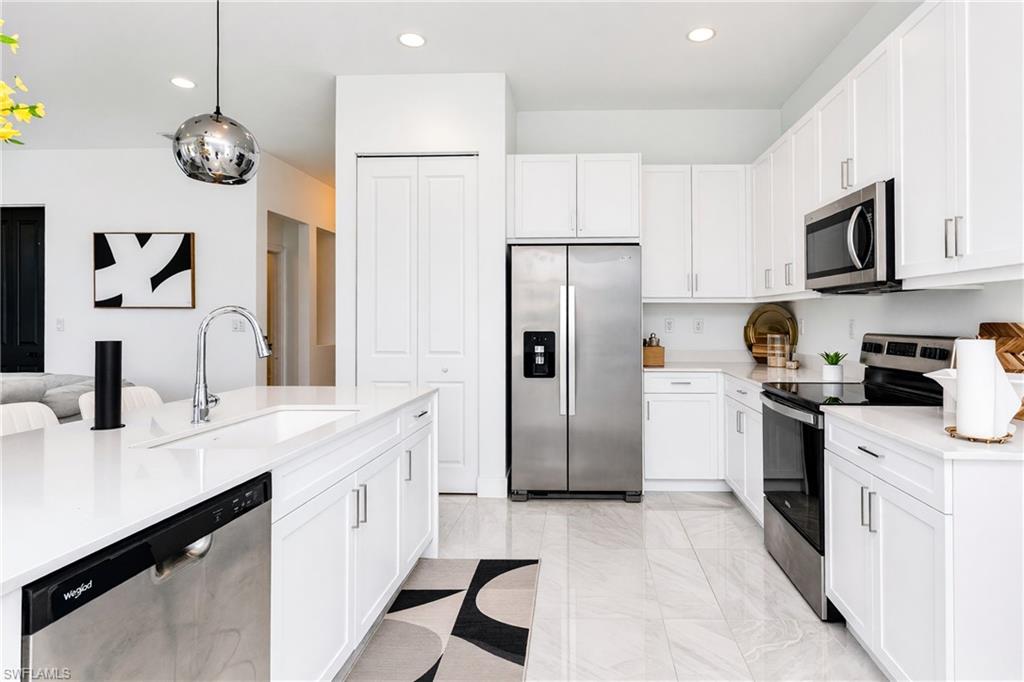 White cabinetry with brushed nickel hardware, stainless steel appliances, a large center island with an integrated sink, white countertops, and light-toned tile flooring