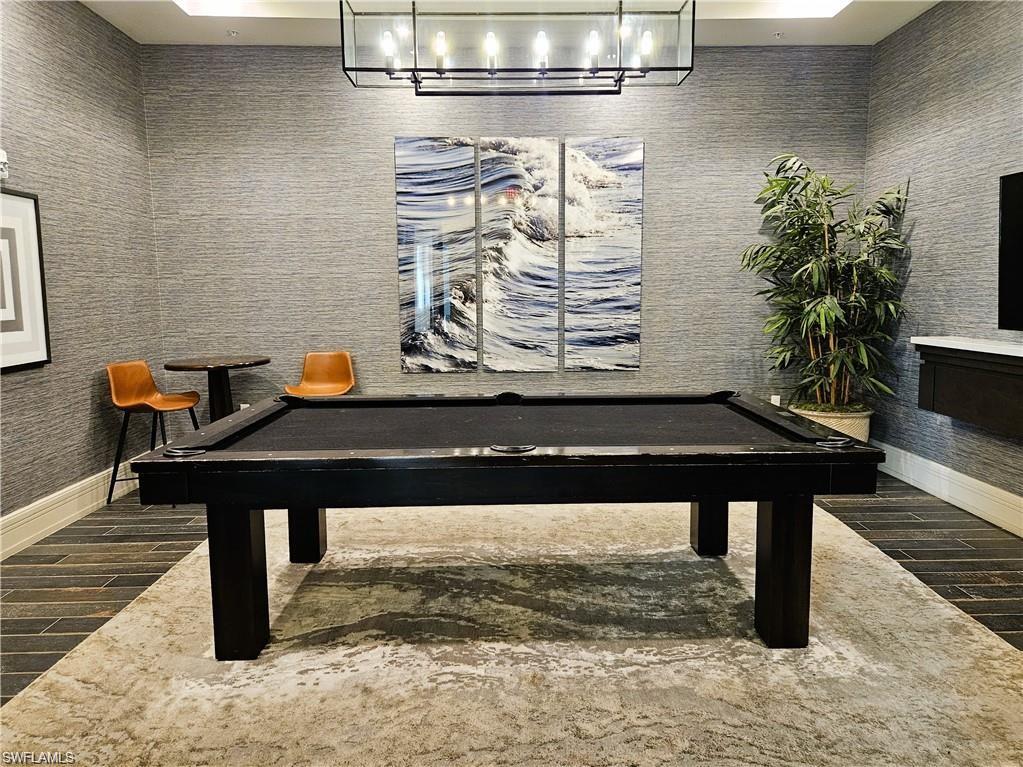 Textured wall covering, linear chandelier, dark wood-finish flooring, built-in floating cabinet, and recessed ceiling lighting