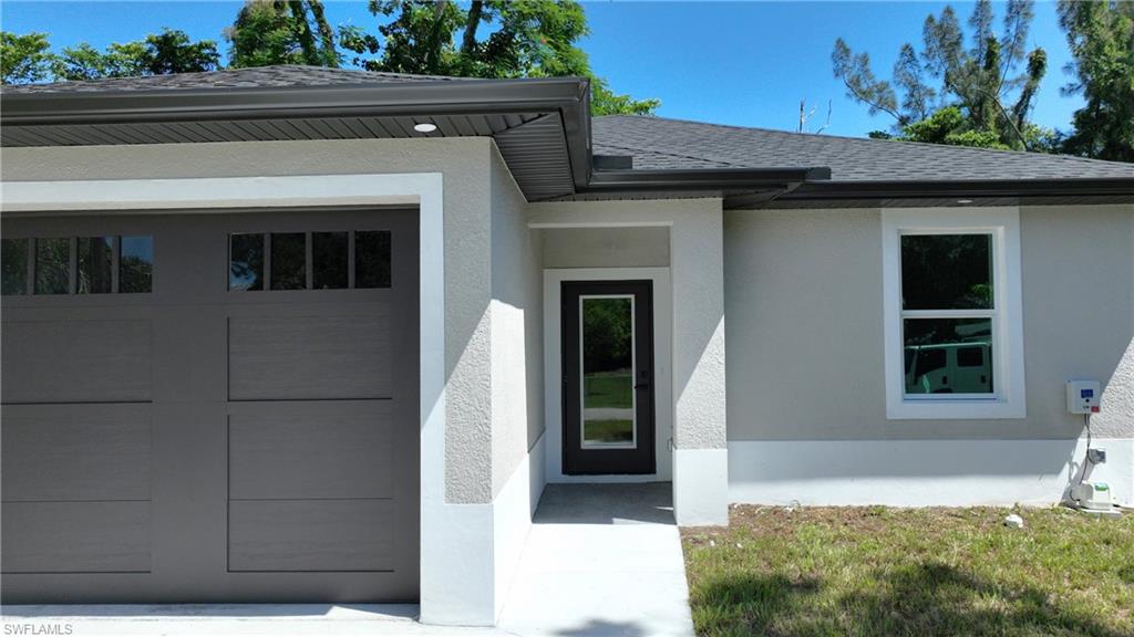 Modern exterior with a neutral stucco finish, dark gray garage door with windows, black-framed front entry door, and white-framed windows