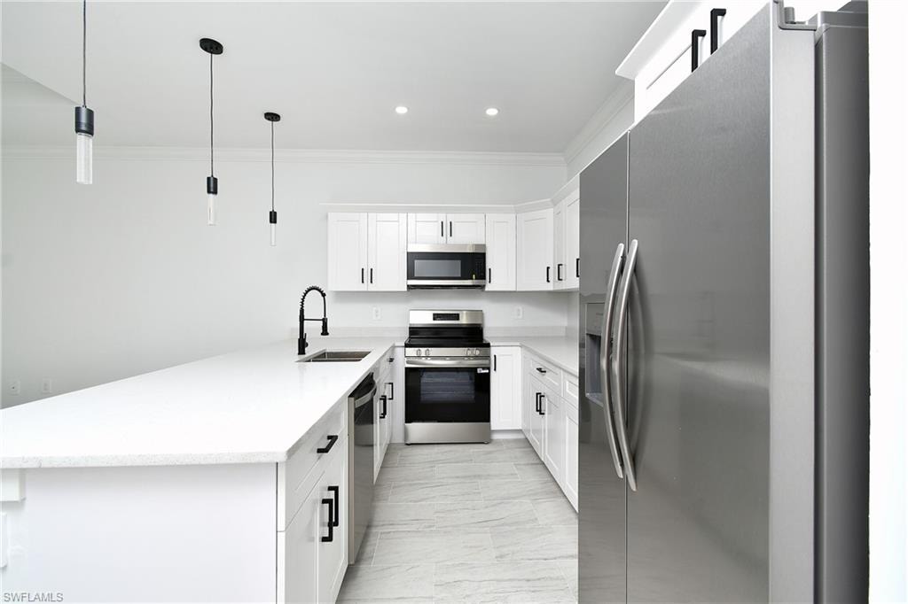 Kitchen featuring white cabinetry, stainless steel appliances, white countertops, and pendant lighting