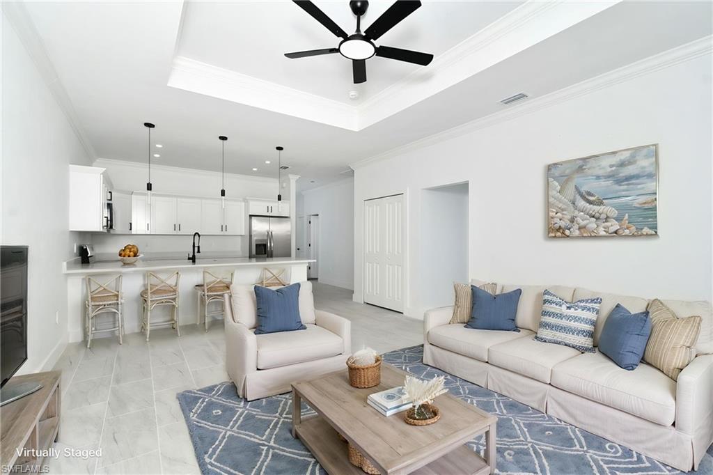 Bright open-concept living space with a recessed tray ceiling, ceiling fan, and light-toned tile flooring