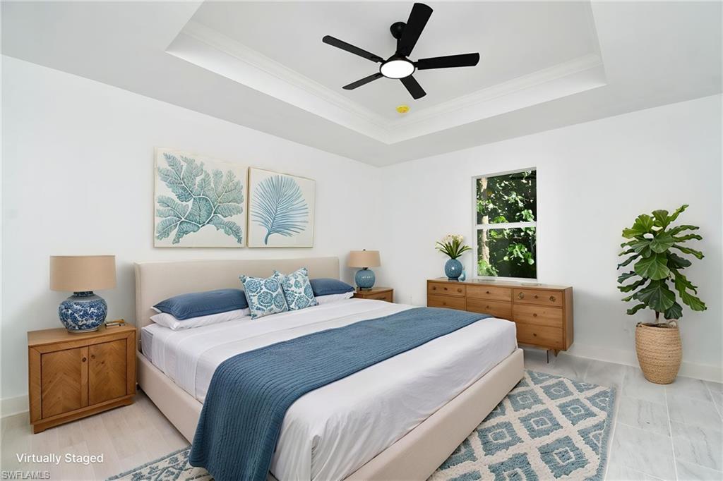 Tray ceiling with crown molding, modern ceiling fan, large window, and light-toned flooring