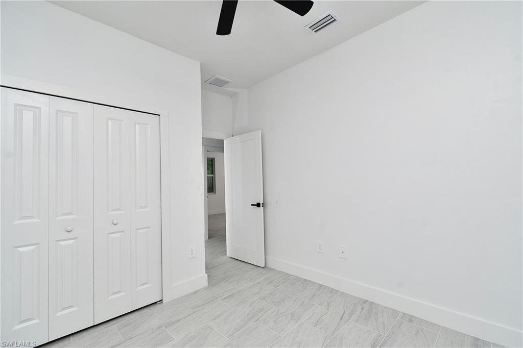 White paneled bi-fold closet doors, light-toned tile flooring, and a black ceiling fan