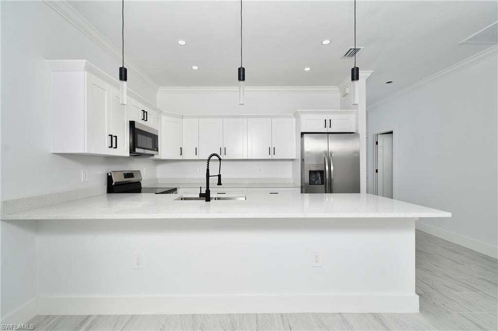 White kitchen featuring an island with a sink, stainless steel appliances, recessed lighting, and pendant lighting fixtures