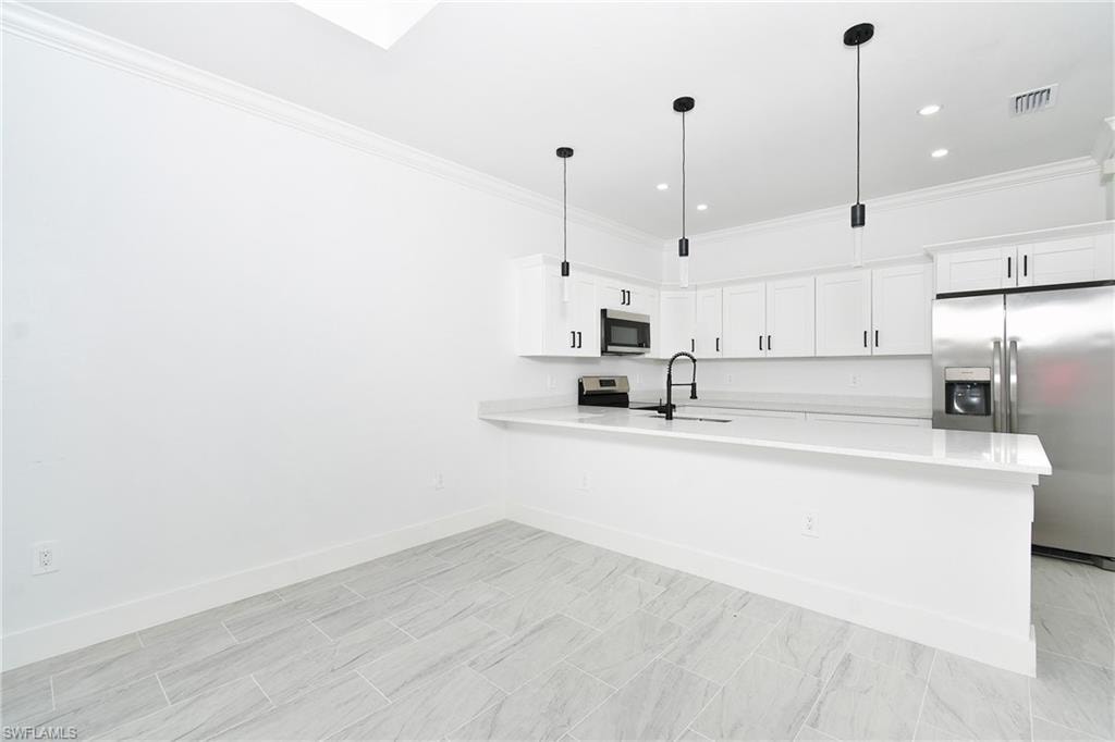 Contemporary kitchen featuring white cabinetry, stainless steel appliances, a breakfast bar, pendant lighting, and light-toned tile flooring