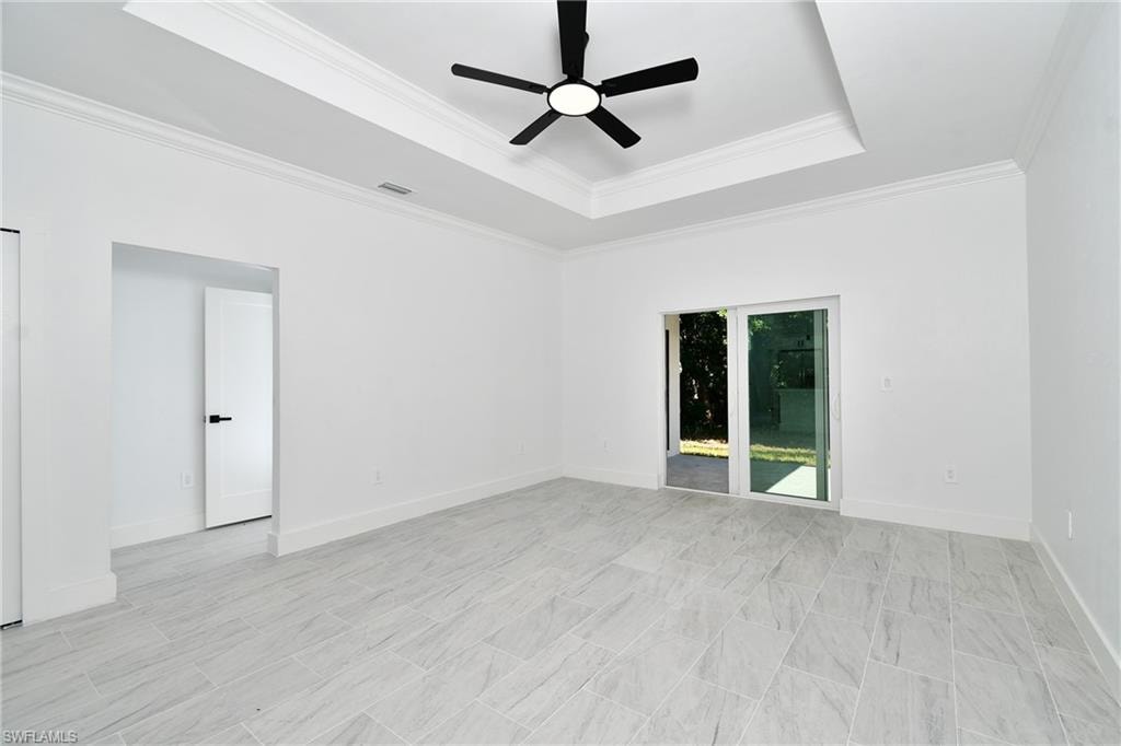 Tray ceiling with crown molding, ceiling fan with integrated lighting, sliding glass door, white interior door with black hardware, and large format tile flooring