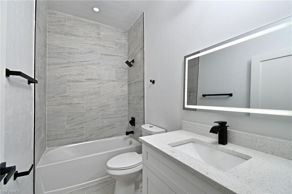 Bathroom featuring a vanity with an integrated sink, solid surface countertop, matte black faucet, and an illuminated mirror
