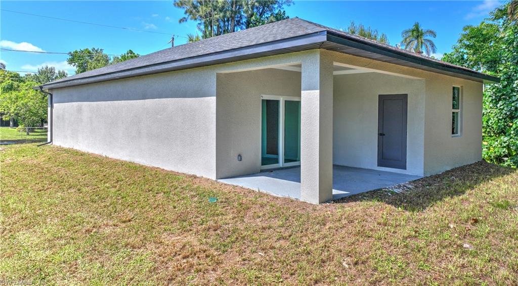 Stucco exterior with a covered patio, dark gray roof, and a single pane window