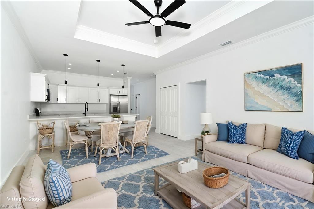 Open-concept living space featuring a tray ceiling with a ceiling fan, white kitchen cabinetry, stainless steel appliances, and a built-in kitchen island